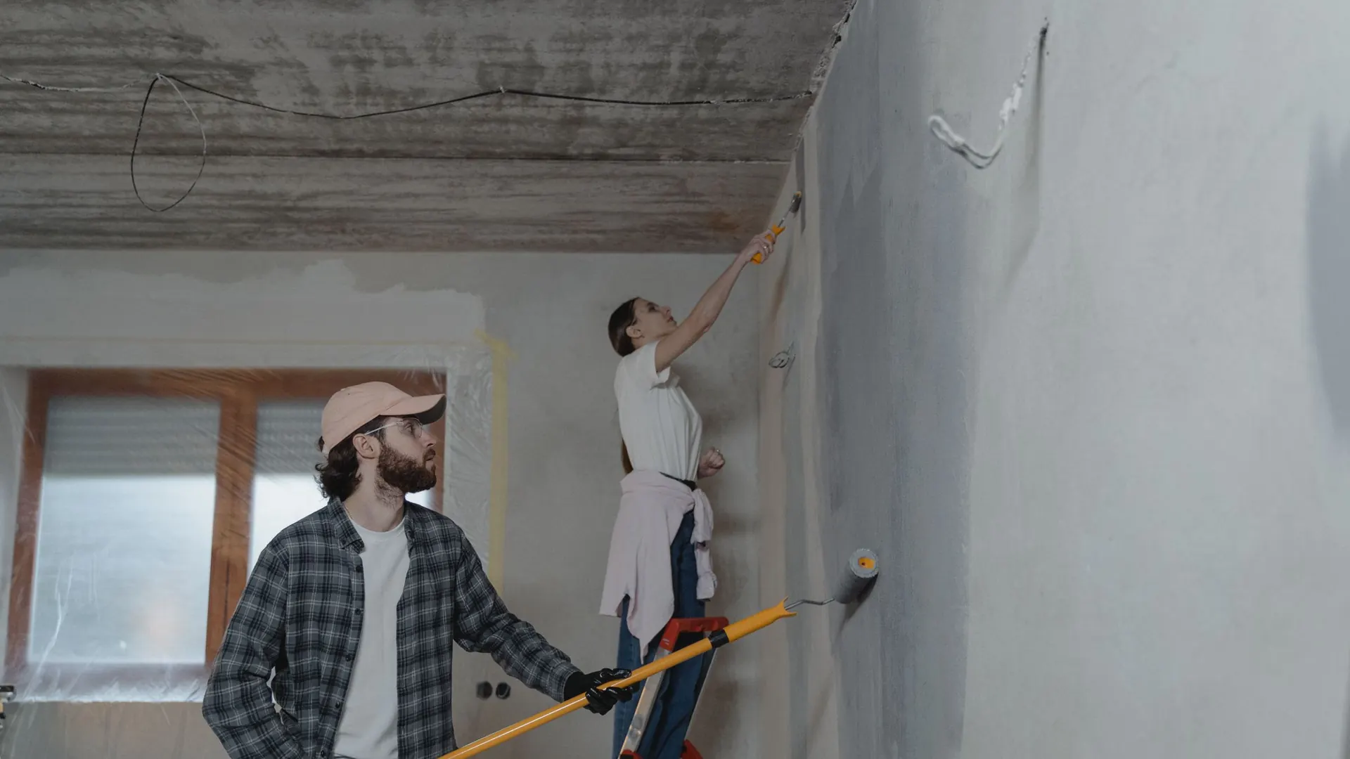 Due persone ristrutturano una stanza con scala e rullo